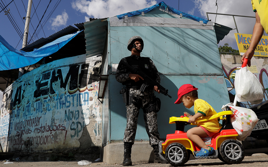 A boy on a cart is pushed near a Brazilian Public-Safety National Force policeman as he patrols an entrance of Chapadao slums complex during a security operation on an effort to crack down on crime in Rio de Janeiro, Brazil. PHOTO: REUTERS