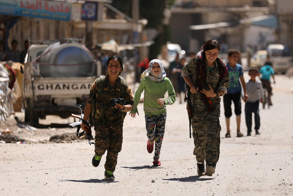 Syrian Democratic Forces (SDF) women fighters run with chidlren in the town of Tabqa, after SDF captured it from Islamic State militants this week, Syria. PHOTO: REUTERS