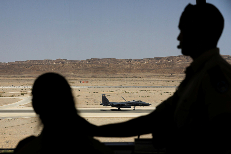 Silhouetted Israeli soldiers work inside a control tower, as a US. F-15 fighter jet is seen in the background, during an exercise dubbed 