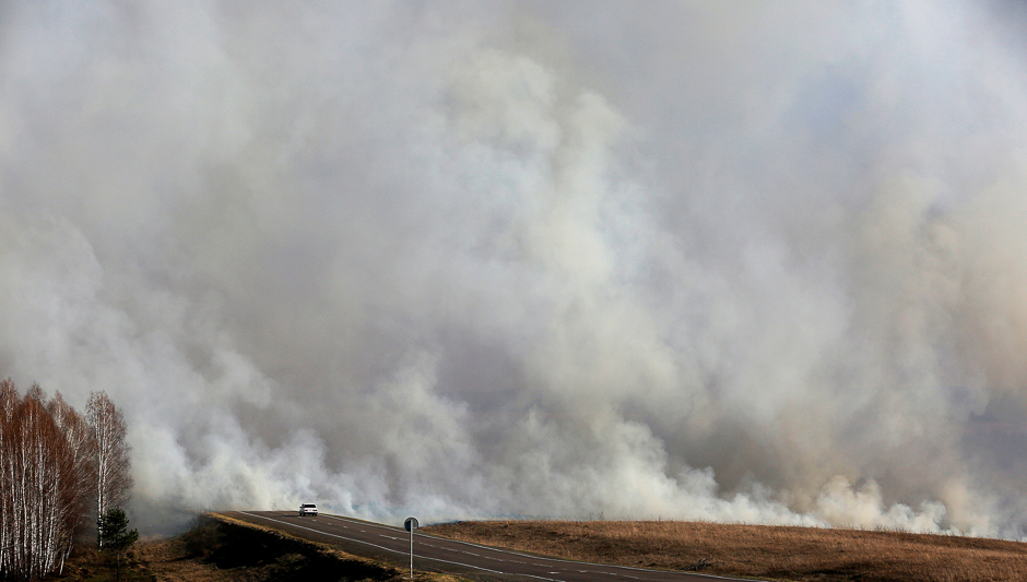 A car drives along the M54 federal highway as smoke rises from burning grass and forest fire, south of Krasnoyarsk, Russia. PHOTO: REUTERS