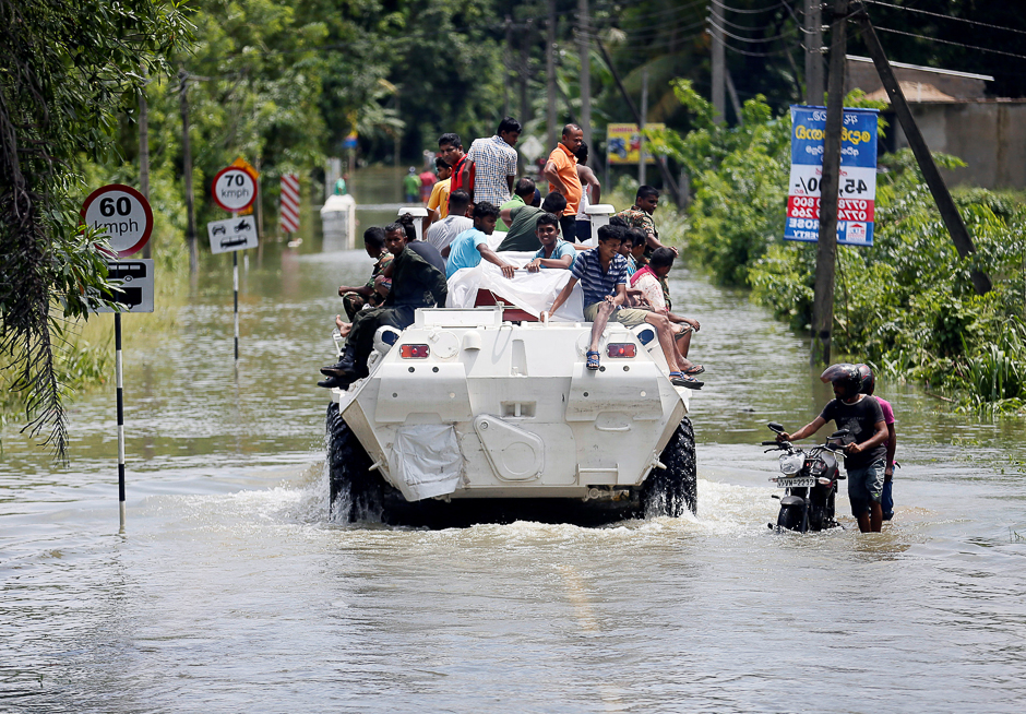 People are transported on top of an armoured personnel carrier on a flooded road as a man pushes his bike thorugh the water, in Bulathsinhala village, in Kalutara, Sri Lanka. PHOTO: REUTERS
