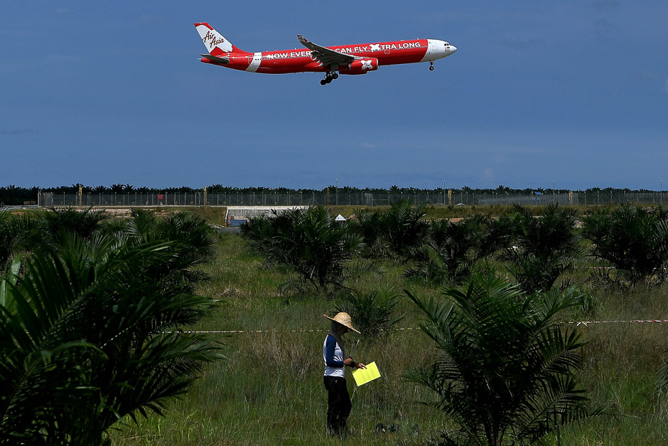 A Malaysian fertilizer research worker works in a field as an AirAsia A333 airbus prepares to land at the Kuala Lumpur International Airport 2 (KLIA 2) in Sepang. PHOTO: AFP