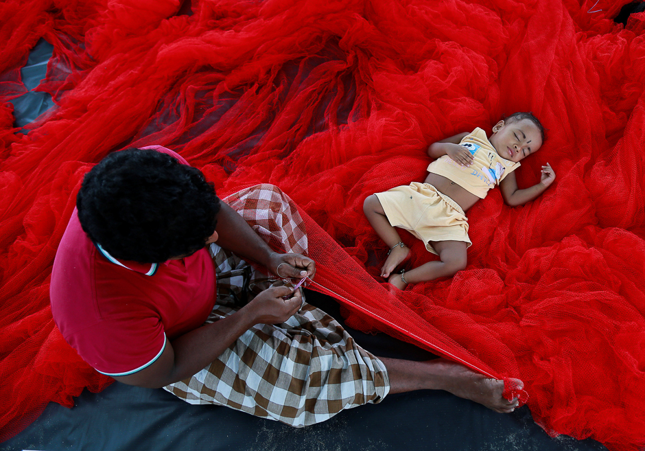A fisherman stitches nets as his child sleeps beside him along the sea coast on the outskirts of Kochi, India. PHOTO: REUTERS