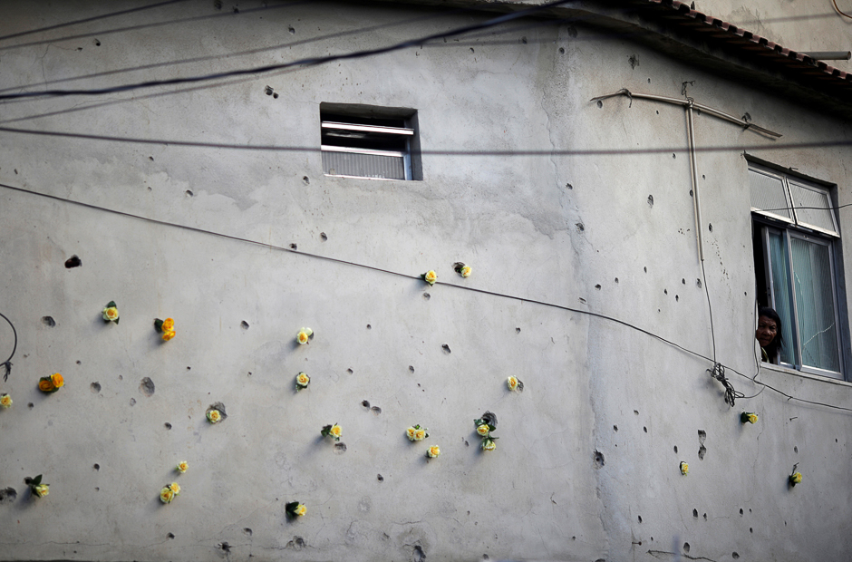 A woman stands at the window of her house, which was damaged by bullets during clashes between drug gangs, as she observes a protest against violence in Mare slums complex in Rio de Janeiro, Brazil. PHOTO: REUTERS