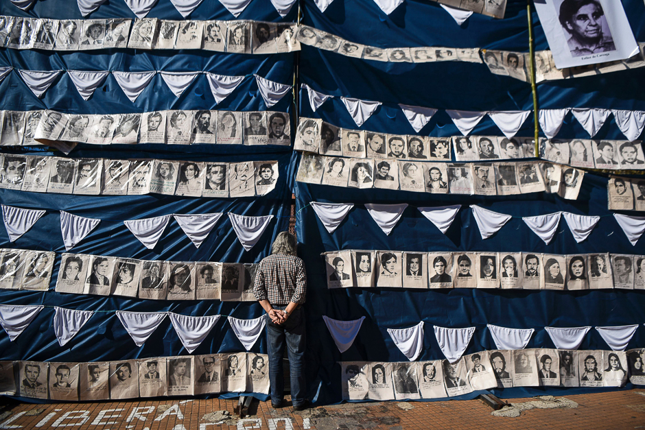 A man peers behind portraits of victims of forced disappearance in the Plaza de Mayo square in Buenos Aires, Argentina. PHOTO: AFP