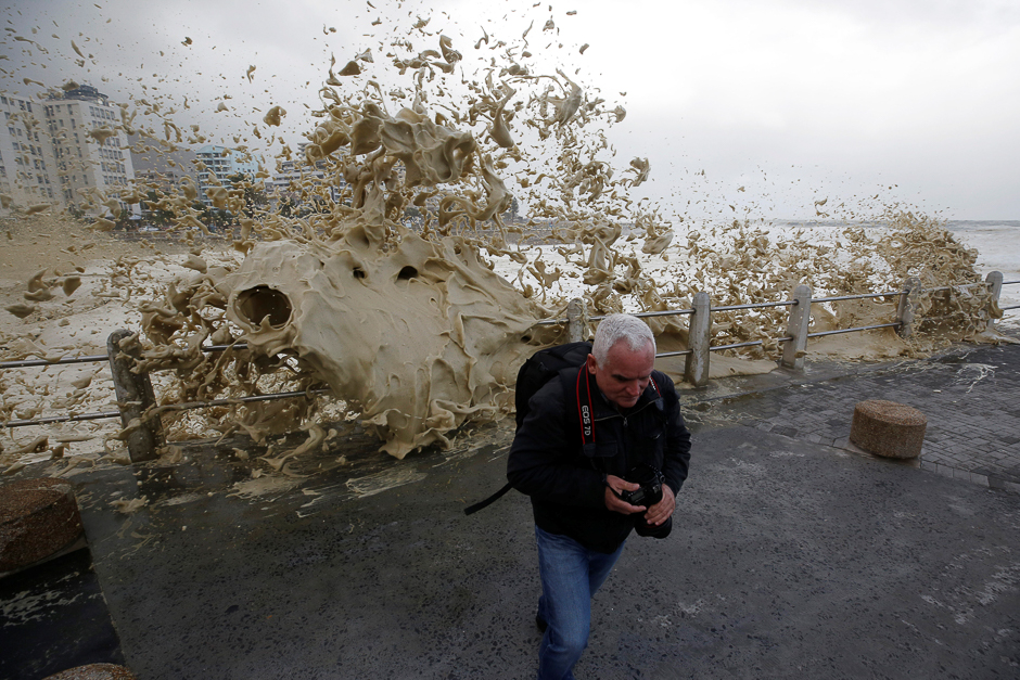 A man runs from sea spray as storms hit Cape Town, South Africa. PHOTO: REUTERS
