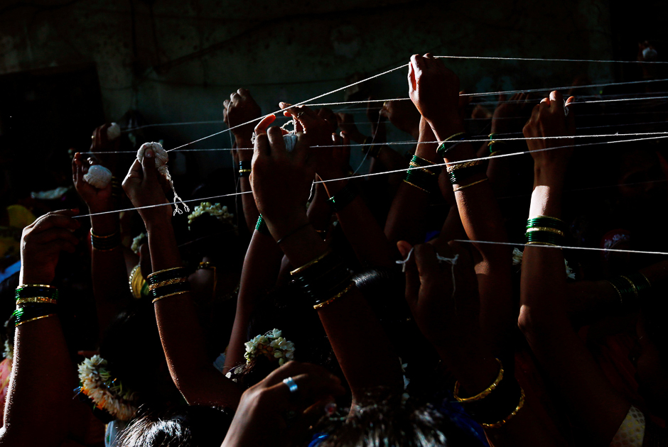 Married Hindu women tie cotton threads around a Banyan tree as they perform rituals on 