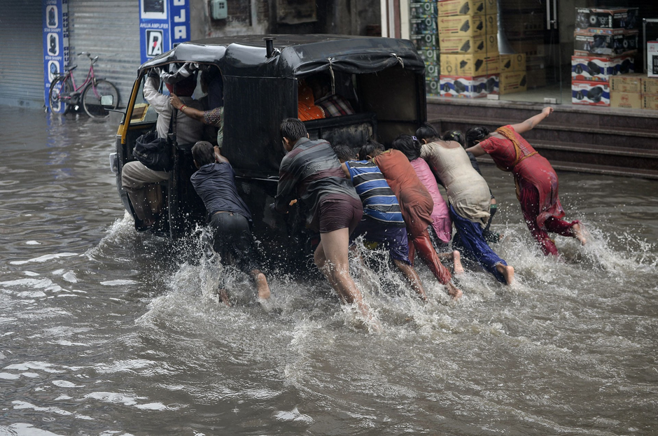 Children push a rickshaw along a flooded street after heavy rain, as the monsoon season begins, India, PHOTO: AFP