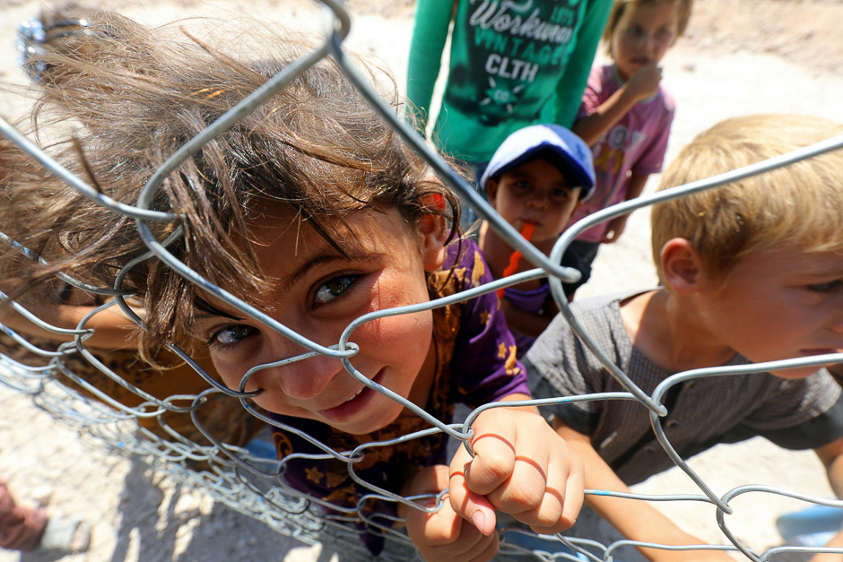 Displaced children from the Islamic State (IS) group's Syrian stronghold of Raqa, pose for a photo behind a fence at a camp in Ain Issa. PHOTO: AFP