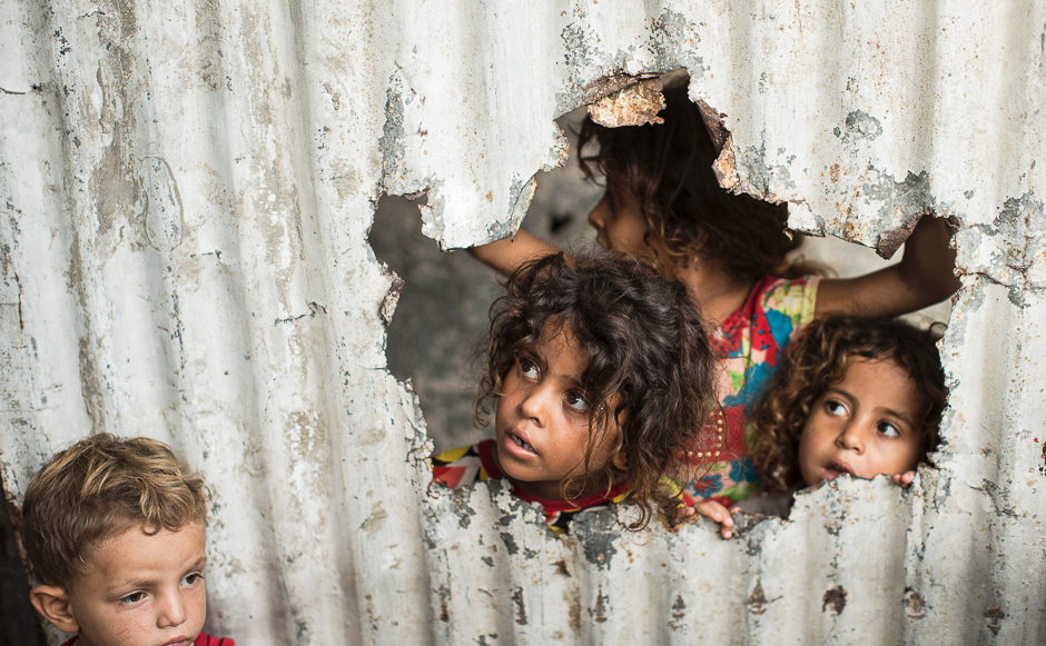 Palestinian children look through a hole in a sheet metal fence outside their home in a poor neighbourhood in Gaza City. PHOTO: AFP