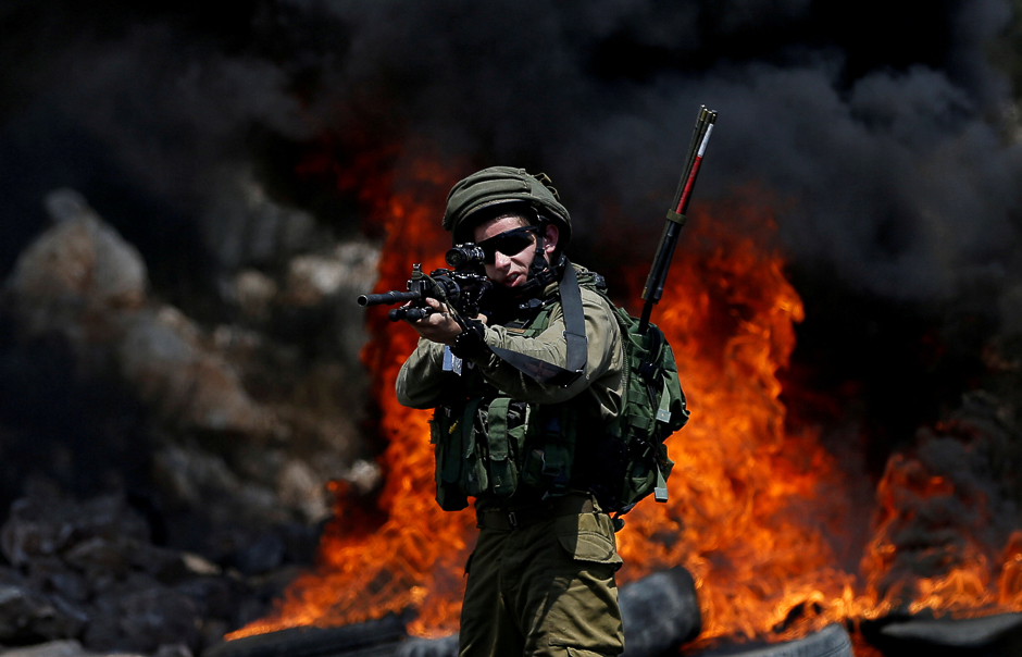 An Israeli soldier walks points his weapon toward Palestinian protesters during clashes in the West Bank village of Kofr Qadom near Nablus. PHOTO: REUTERS