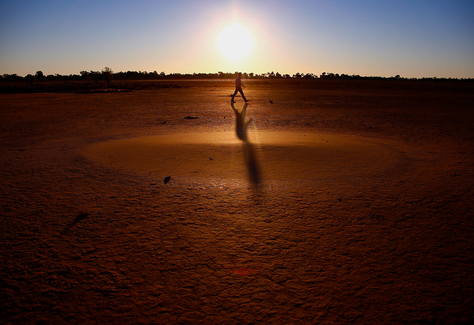 Farmer Tony Reid casts a shadow as he walks across a claypan while inspecting a paddock on Kahmoo Station property, located Cunnamulla, Australia. PHOTO: REUTERS