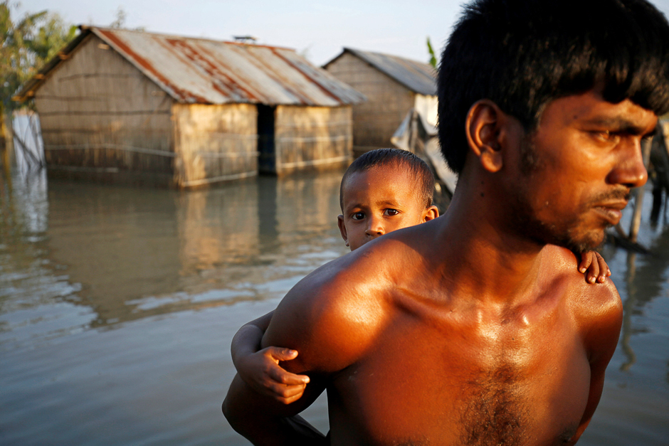 A child reacts to the camera while sitting on his father back as they make their way in a flooded area in Bogra, Bangladesh. PHOTO: REUTERS