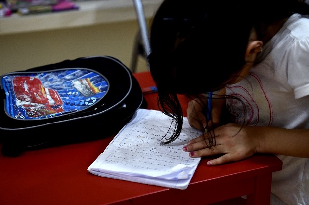 A refugee girl writes at a library set up on the premises of an international non-governmental organisation (NGO) hosting Syrian and Afghan women and children, in central Athens. PHOTO: AFP