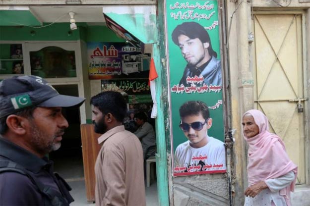 A policeman (L) and residents walk past a shop displaying the pictures of men, who were killed in a suicide blast on January 2015, in a Shia mosque in Shikarpur. PHOTO: REUTERS