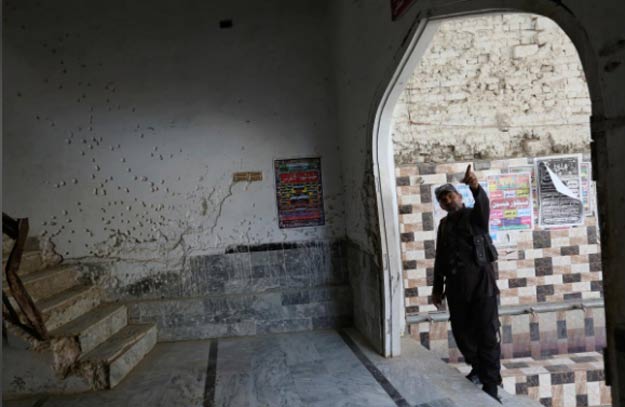 A policeman gestures beside a wall with shrapnel-scars, which witnesses said was damaged in a suicide blast on January 2015, in a Shia mosque in Shikarpur. PHOTO: REUTERS