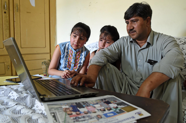 In this photograph Laeeq Shah, the father of Noreen -- who was killed by a stray bullet during celebratory gunfire when Pakistan won the ICC Champions trophy against its arch rival India -- looks at photographs on a computer alongside his daughters at his residence in the northwestern town of Nowshera, in Khyber Pakhtunkhwa province. PHOTO: AFP