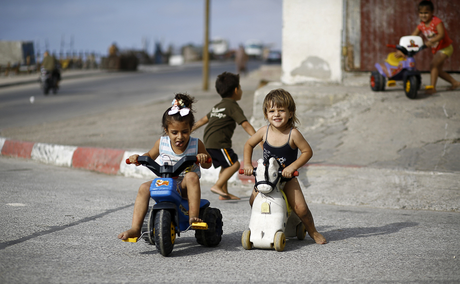 A Palestinian girl rides on a toy tricycle next to another child riding on a wheeled-toy pony in a street near their home in Gaza City. PHOTO: AFP