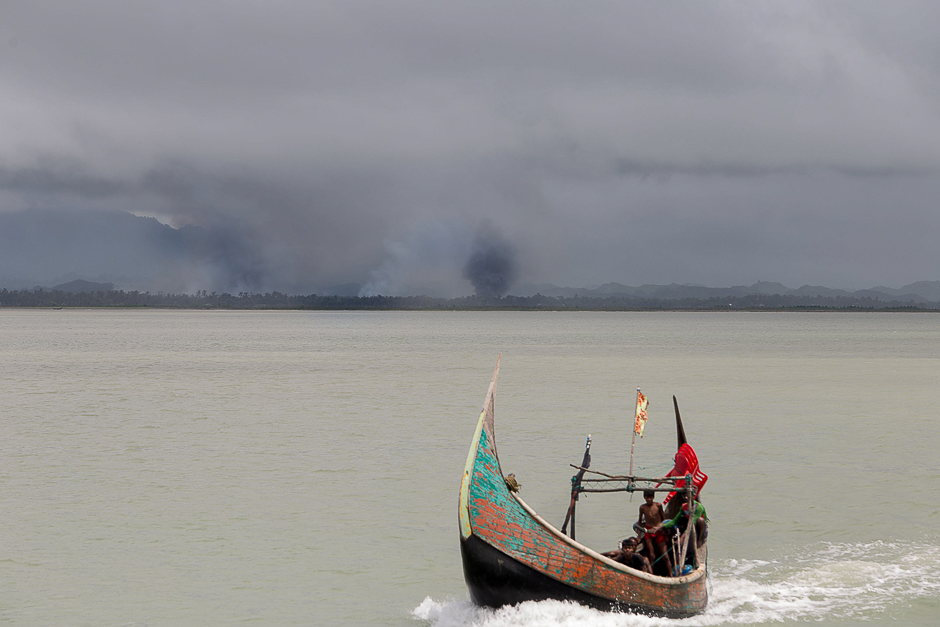 Rohingya refugees arrive by boat, as smoke rises from fires on the shoreline behind them, at Shah Parir Dwip on the Bangladesh side of the Naf River after fleeing violence in Myanmar. PHOTO: AFP