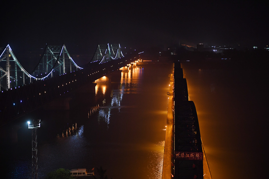 Lights are seen in the North Korean town of Sinuiju, behind the Friendship Bridge (L) which connects Sinuiju and the the Chinese border city of Dandong, and the Broken Bridge (R), in Dandong, in China. PHOTO: AFP