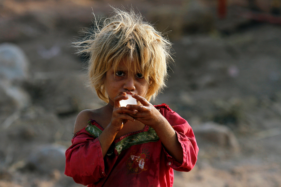 A girl eats a piece of ice as she stands outside her family tent on the outskirts of Peshawar. PHOTO: REUTERS