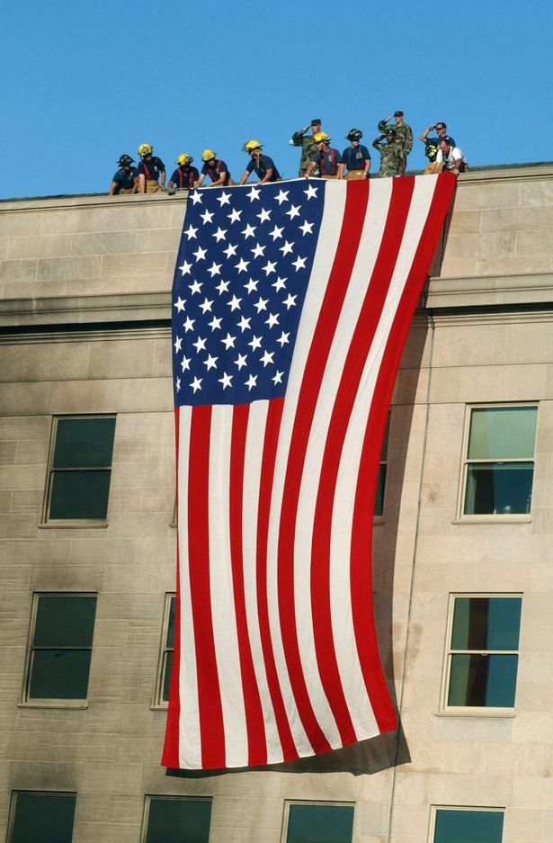 Soldiers from the 3rd Infantry Regiment (The Old Guard) render honors as firefighters and rescue workers unfurl a huge American flag over the side of the Pentagon. PHOTO: US Navy