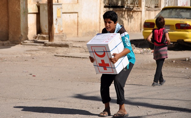 A Syrian child, resident of the northeastern city of Deir Ezzor, carries an aid parcel provided by the Syrian Red Crescent. PHOTO: AFP