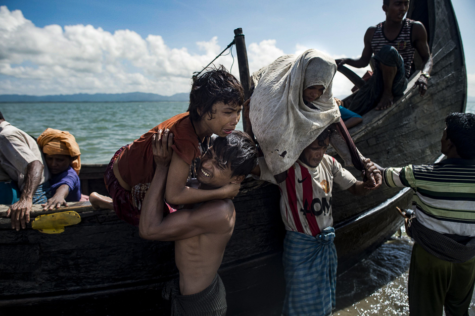 Bangladeshi men help Rohingya Muslim refugees to disembark from a boat on the Bangladeshi shoreline of the Naf river after crossing the border from Myanmar in Teknaf. PHOTO: AFP