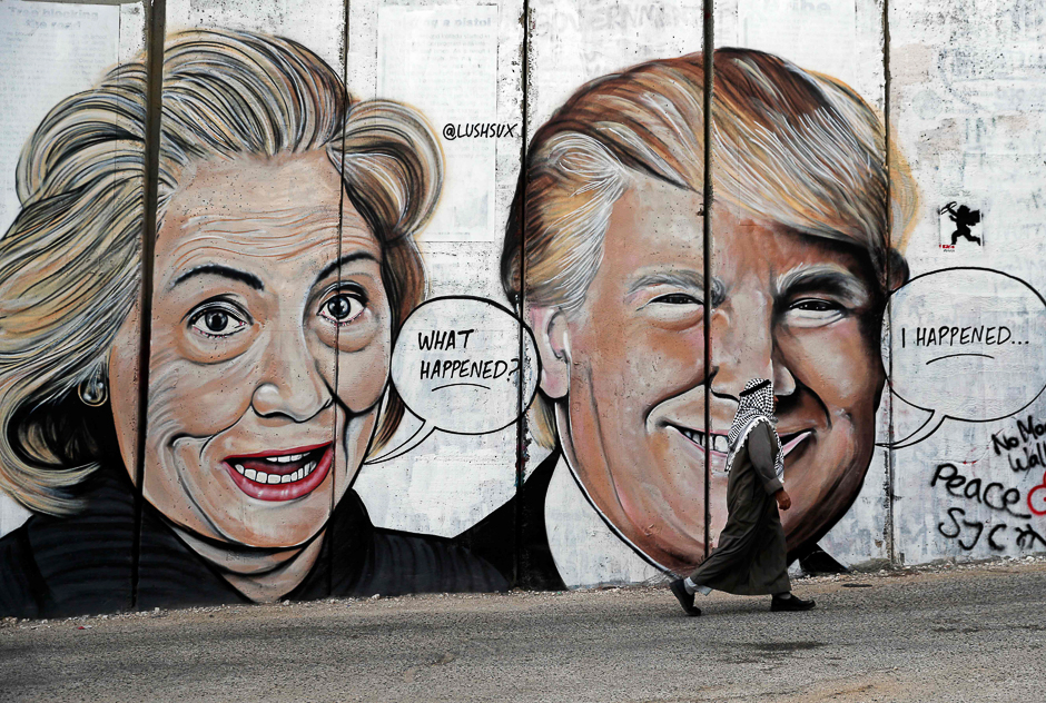 A Palestinian man walks past a newly sprayed graffiti depicting US presidential candidate Hillary Clinton and US President Donald Trump on the controversial Israeli separation wall separating the West Bank town of Bethlehem from Jerusalem. PHOTO: AFP