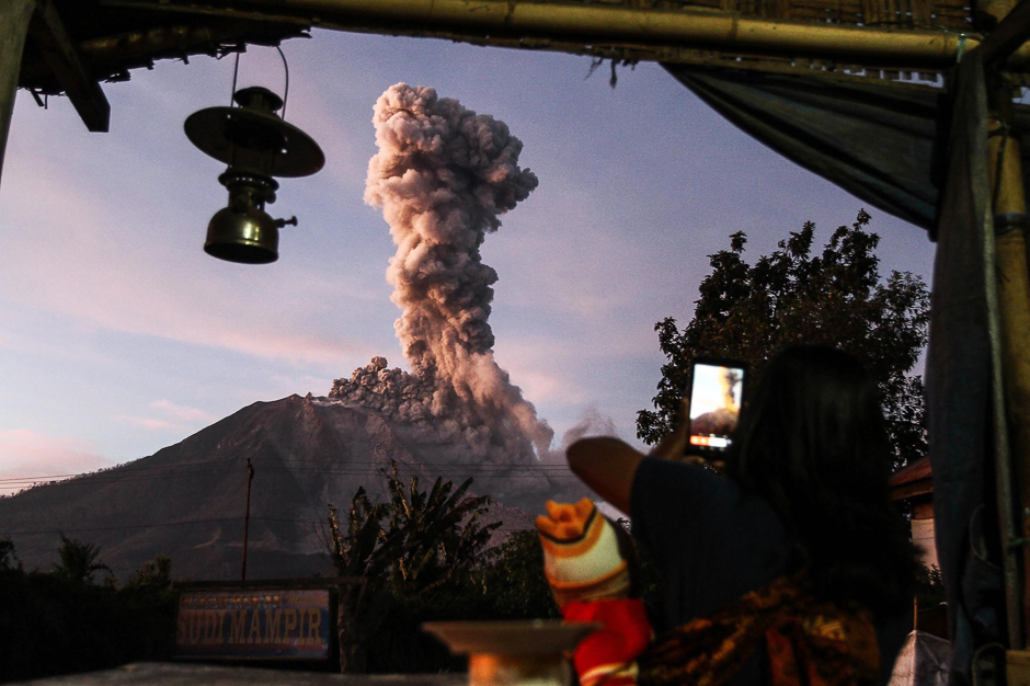 An Indonesian villager takes a picture of Mount Sinabung volcano as it spews thick smoke as seen from Tiga Pancur village in Karo, North Sumatra. PHOTO: AFP