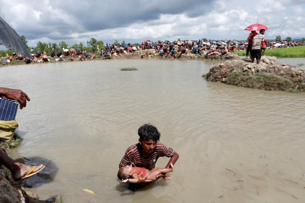 A Rohingya refugees walks with a baby in a rice field after crossing the border in Palang Khali, Bangladesh October 9, 2017. PHOTO: REUTERS