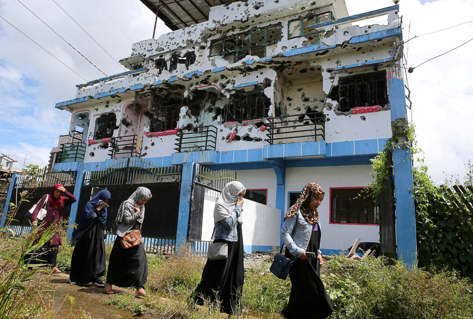 Residents who returned from evacuation centres walk past a bullet-ridden house in Basak, Malutlut district in Marawi city, Philippines. PHOTO: REUTERS