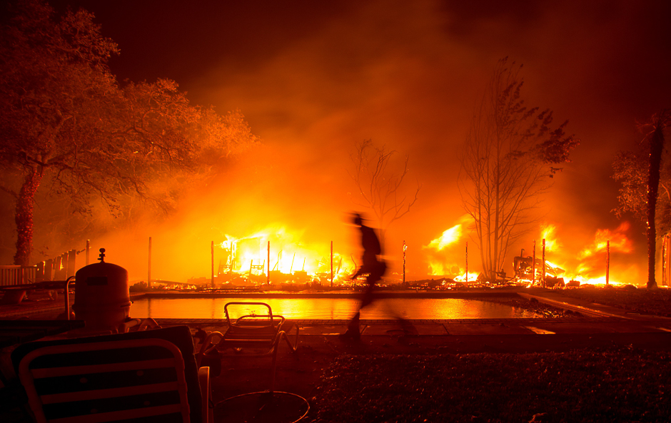 A firefighter walks near a pool as a neighboring home burns in the Napa wine region in California as multiple wind-driven fires continue to whip through the region. PHOTO: AFP