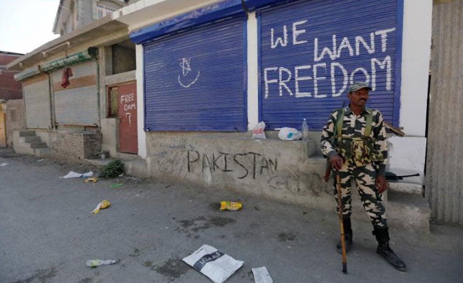 An Indian policeman stands guard near shops painted with graffiti during a curfew in Srinagar, August 5, 2016. PHOTO: REUTERS