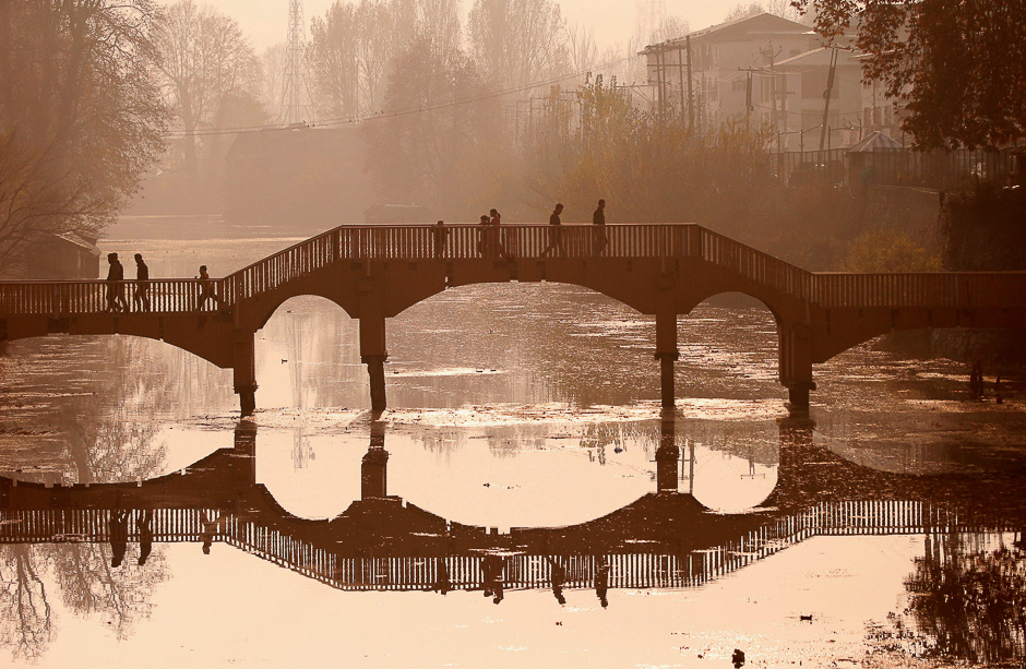 People walk on a wooden footbridge across a canal during an autumn day in Srinagar. PHOTO: REUTERS
