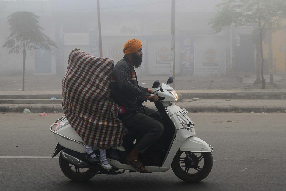 Indian schoolgirls are covered in a sheet in an effort to protect themselves from heavy smog as they are driven to school on a scooter after three days off due to the air pollution in Amritsar. PHOTO: AFP
