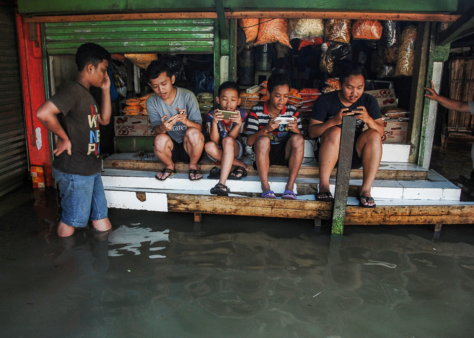 Indonesian youths sit on a table while playing games at a game centre surrounded by floodwaters after seasonal rains hit the area around Bandung, West Java province. PHOTO: AFP