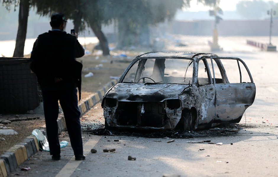 A policeman takes a picture of a car burned during clashes near the Faizabad junction in Islamabad. PHOTO: REUTERS