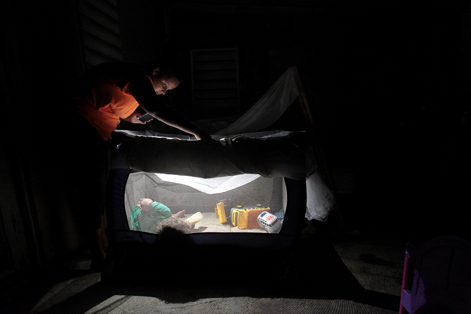 A woman uses a flashlight as she looks at her child lying in a cot, after Hurricane Maria hit the island in September and damaged the electrical grid, in Dorado, Puerto Rico. PHOTO: REUTERS