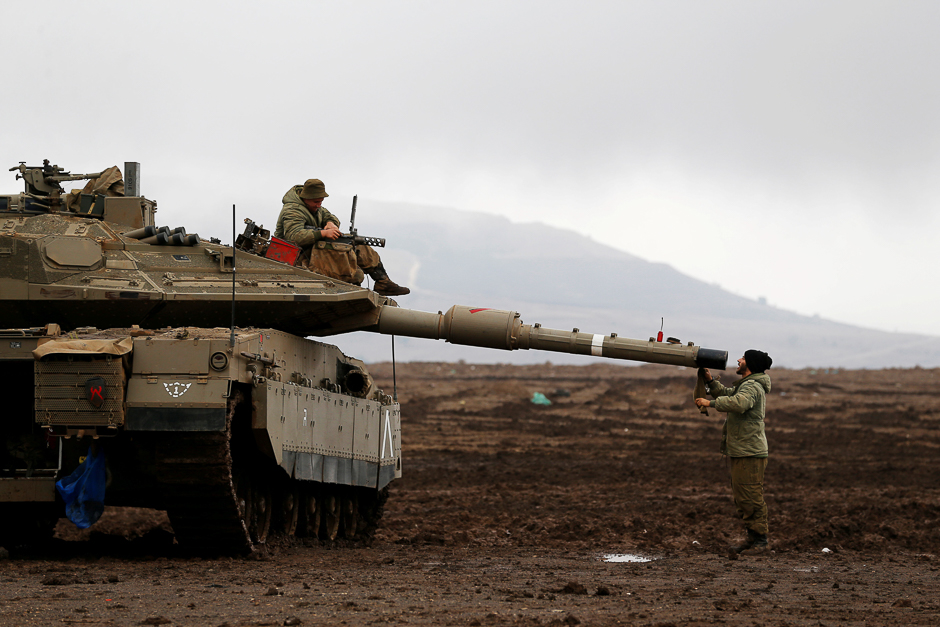 An Israeli soldier sits atop a tank and his comrade stands nearby in the Israeli-occupied Golan Heights, close to Israel's frontier with Syria. PHOTO: REUTERS