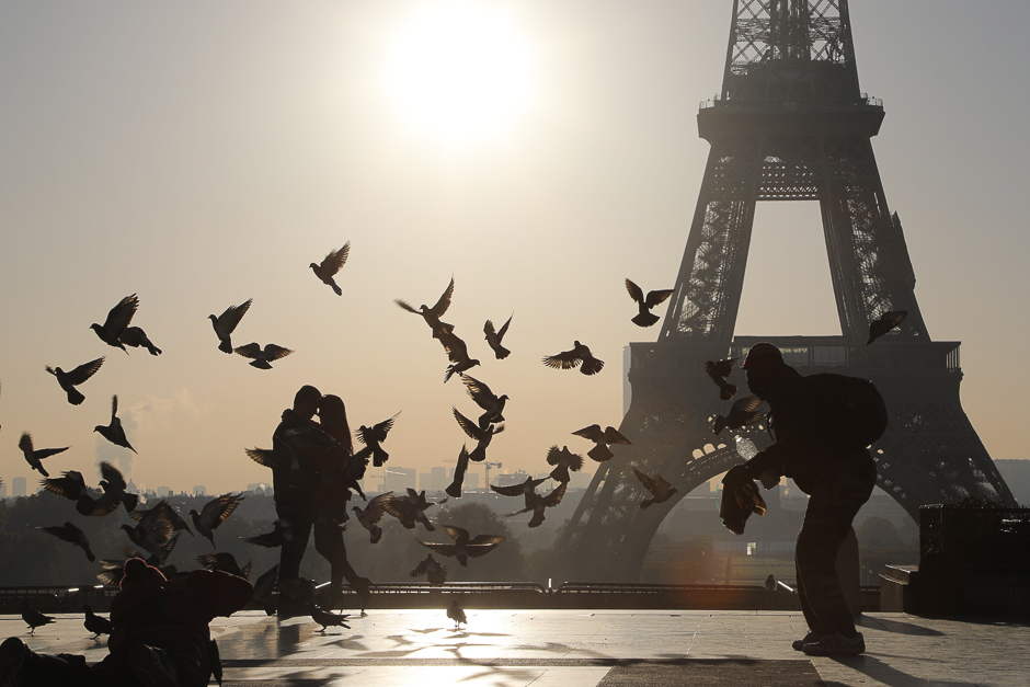 A couple poses for a photographer (L) as a flock of pigeons takes off on the Trocadero plaza opposite the Eiffel Tower, at sunrise in Paris. PHOTO: AFP