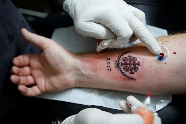 Tattoo artist, Wassim Razzouk, who is continuing his family's tradition of inking Christian pilgrims with ancient tattoos, completes a tattoo on a customers arm at his studio in Jerusalem's Old City November 27, 2017. Picture taken November 27, 2017. PHOTO: REUTERS