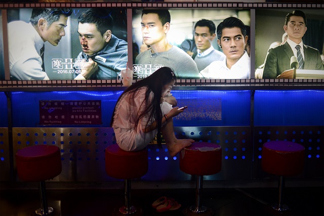 this file picture taken on august 30 2016 shows a woman looking at her mobile phone at the entrance of a cinema in beijing a chinese simulation game quot love and producer quot that has been downloaded more than 10 million times since debuting in december mostly by women seeking steamy fantasy affairs with its four virtual suitors photo afp