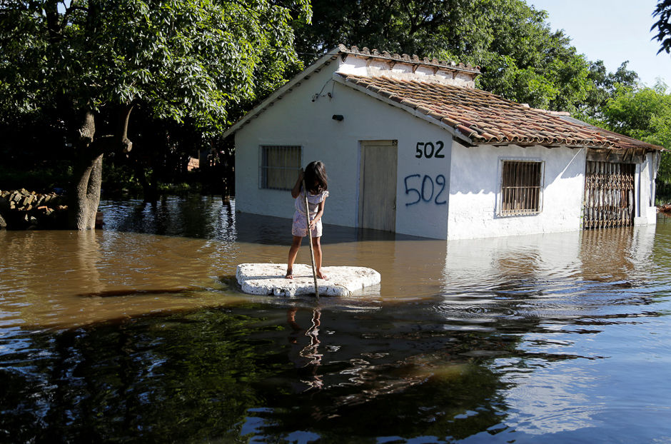 A young girl uses a piece of styrofoam as a paddle board next to a flooded home after heavy rains caused the river Paraguay to overflow, on the outskirts of Asuncion, Paraguay. PHOTO: REUTERS