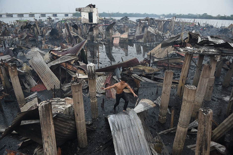A resident walks on a galvanised roof sheet and destroyed homes after a fire hit at an informal settlers area along the coast in Bacoor town, Cavite province, southwest of Manila. PHOTO: AFP