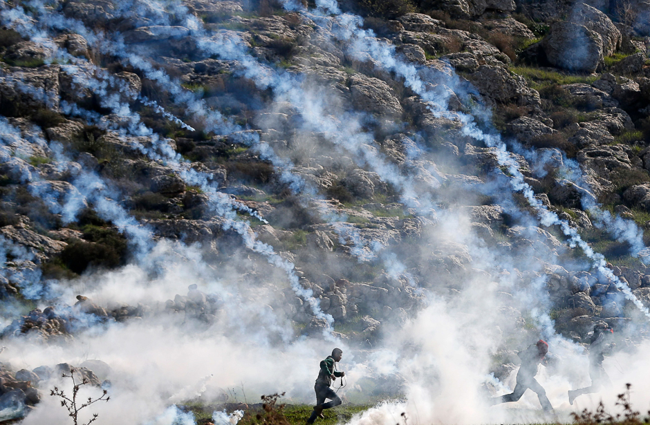 Palestinians run for cover from tear gas during clashes with Israeli soldiers in the village of Mugheer, about 25 kilometres northeast of the city of Ramallah, in the occupied West Bank. PHOTO: AFP