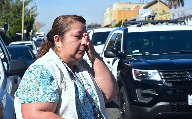 A parent reacts while crossing the street past police vehicles outside a roadblock to Salvadore Castro Middle School in Los Angeles, California. PHOTO: AFP