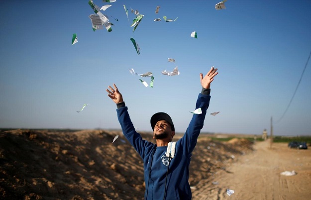 A Palestinian man throws leaflets dropped by the Israeli military during a protest against the U.S. embassy move to Jerusalem and ahead of the 70th anniversary of Nakba, at the Israel-Gaza border, east of Gaza City May 14, 2018. REUTERS/Mohammed Salem