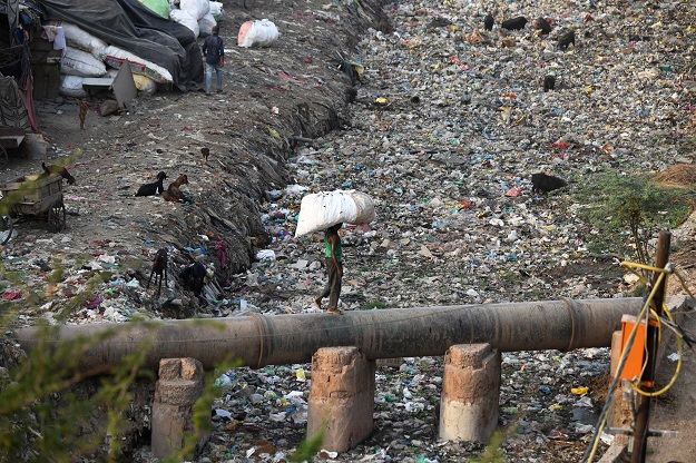 This photo taken on May 30, 2018 shows a man carrying a bag containing plastic recyclable items as he walks on a water pipe next to a sewage drain canal full of garbage in the Taimur Nagar slum area in New Delhi. A sea of plastic spreads through the New Delhi slum of Taimur Nagar, a symbol of the grime and waste that makes the Indian capital one of the world's most polluted cities. India is to be the focus of World Environment Day on June 5, but it is far from the minds of the long-suffering inhabitants of Taimur Nagar. PHOTO: AFP