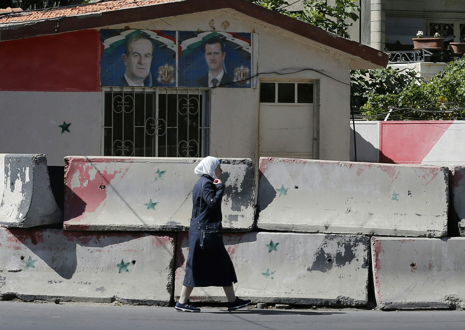 A Syrian woman walks past cement blocks on the side of the road on July 10, 2018 after a security barrier was removed from the area in Damascus. PHOTO: AFP.